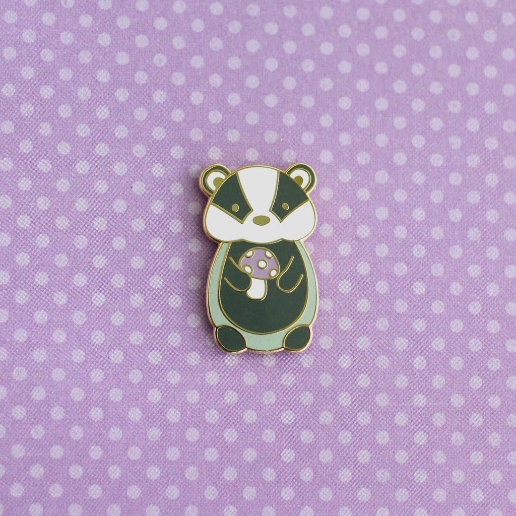Pin's en émail représentant un blaireau tenant un champignon violet - Pin's animal mignon