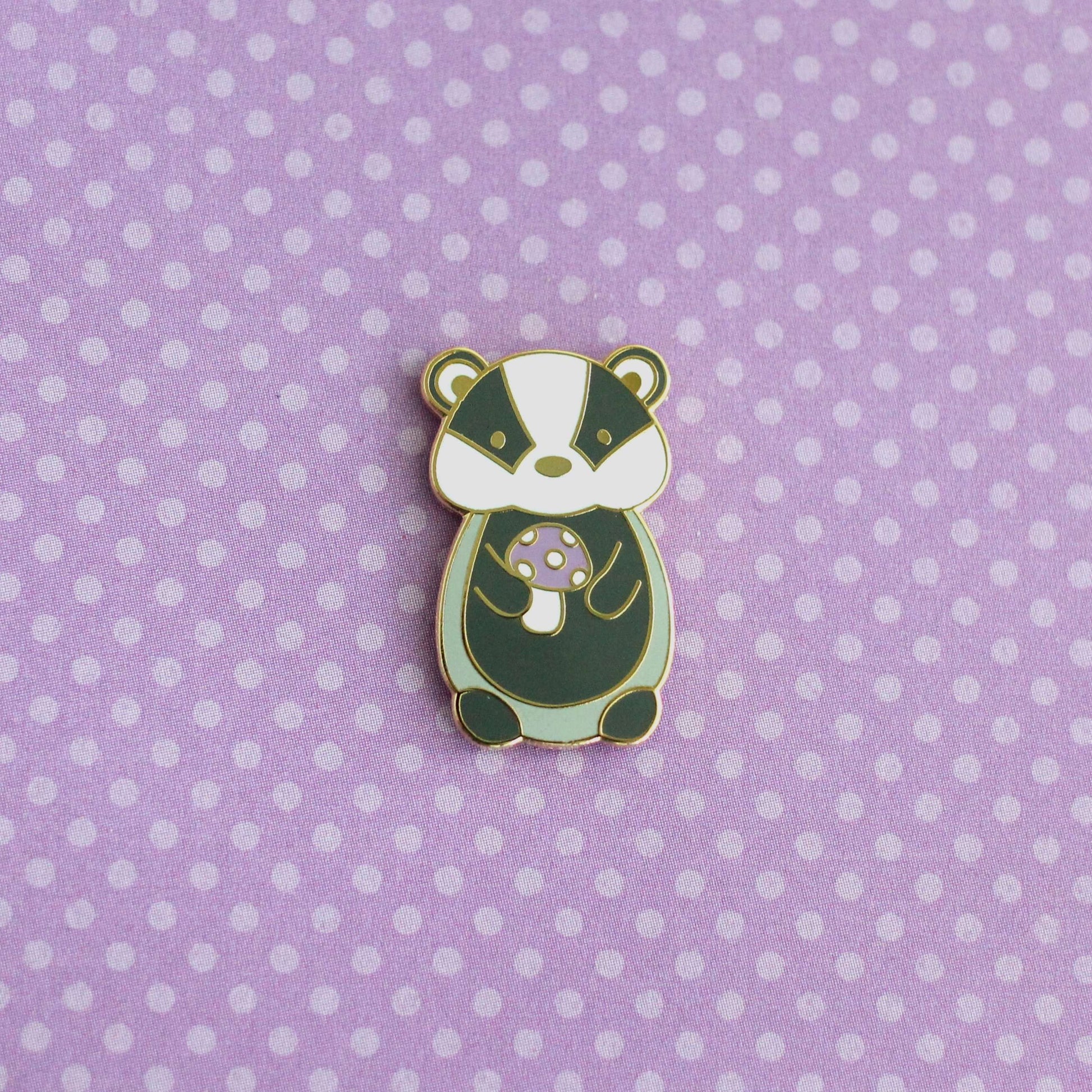Pin's en émail représentant un blaireau tenant un champignon violet - Pin's animal mignon