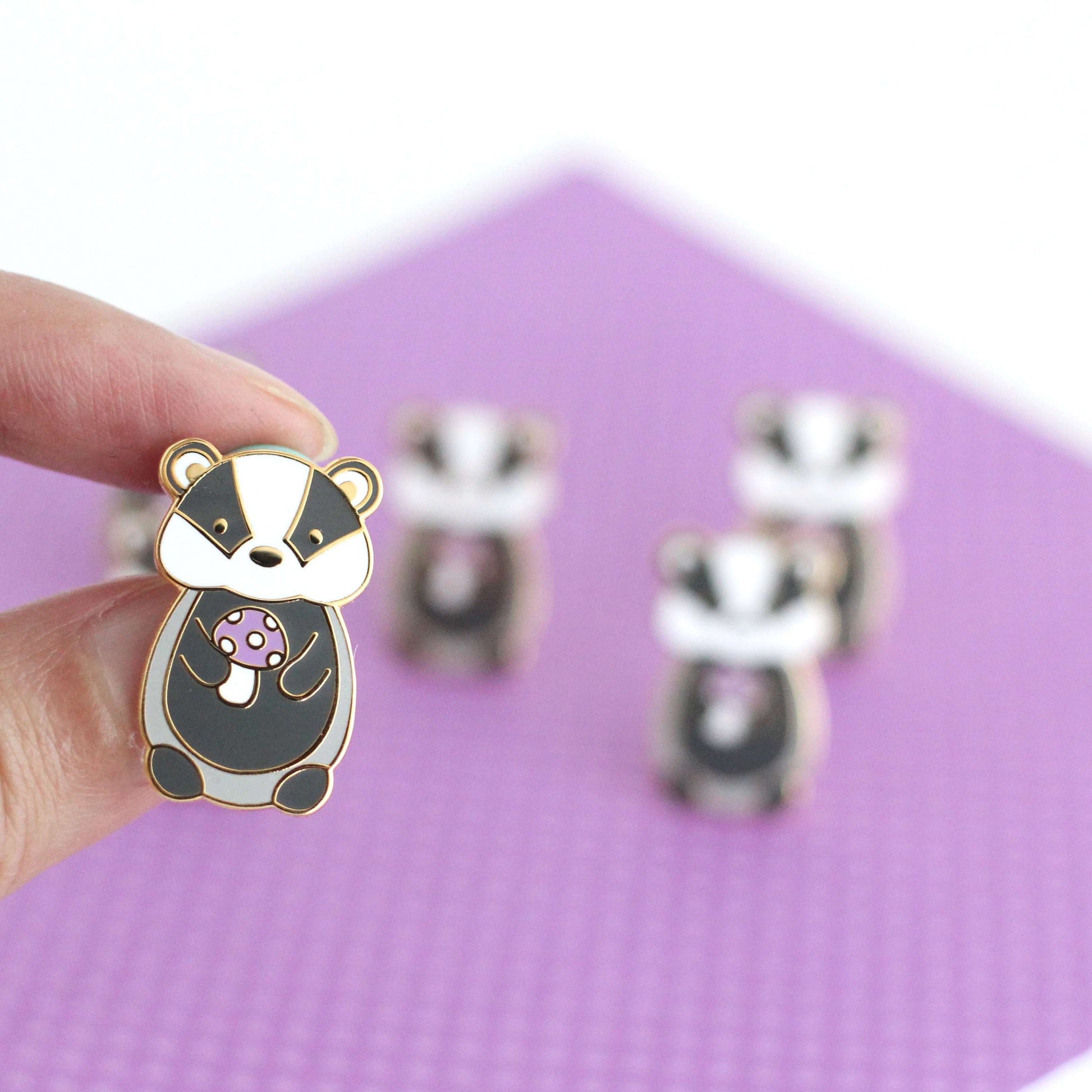 Pin's en émail représentant un blaireau tenant un champignon violet - Pin's animal mignon