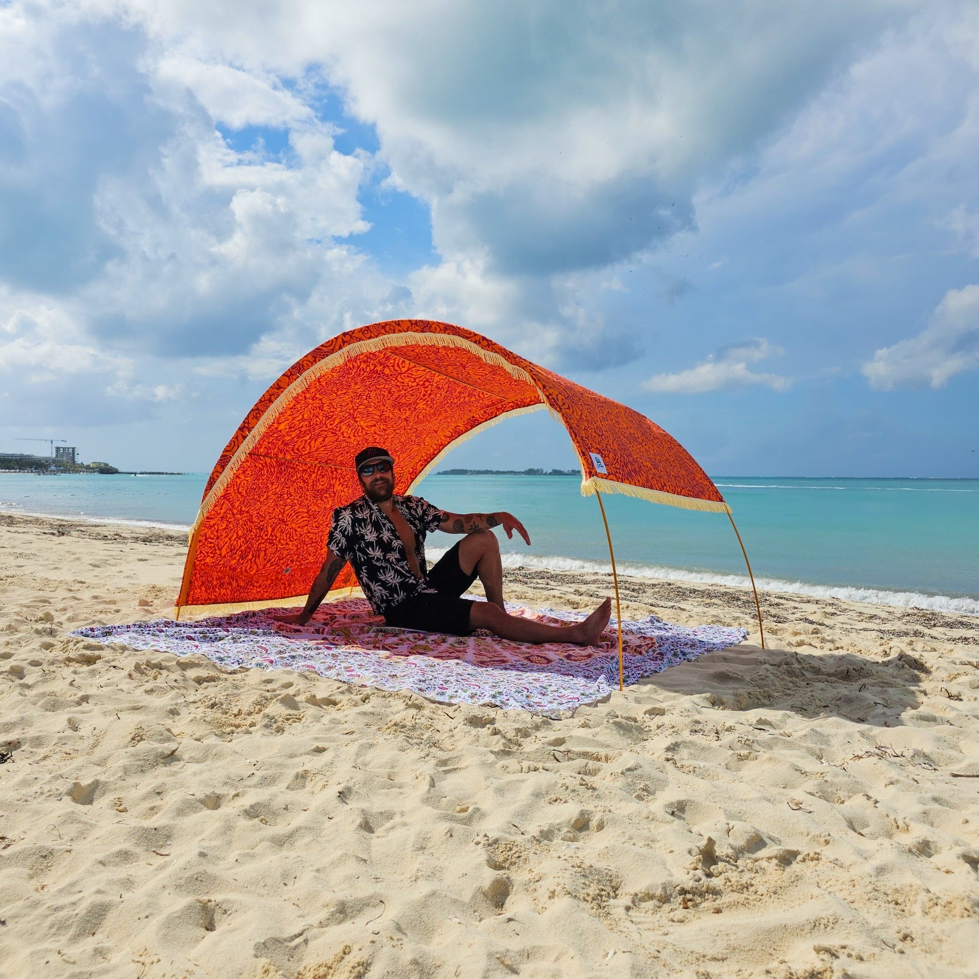 Suniela Tribal Jungle beach cabana with adjustable canopy pulled to one side for targeted sun protection, set up on the sand with a person relaxing underneath.
