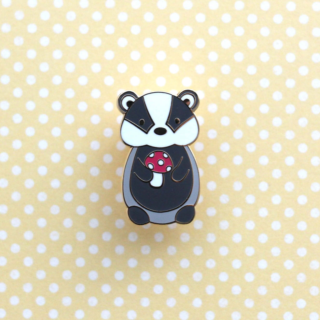 Badge en émail représentant un blaireau tenant un champignon rouge. Badge animal des bois.