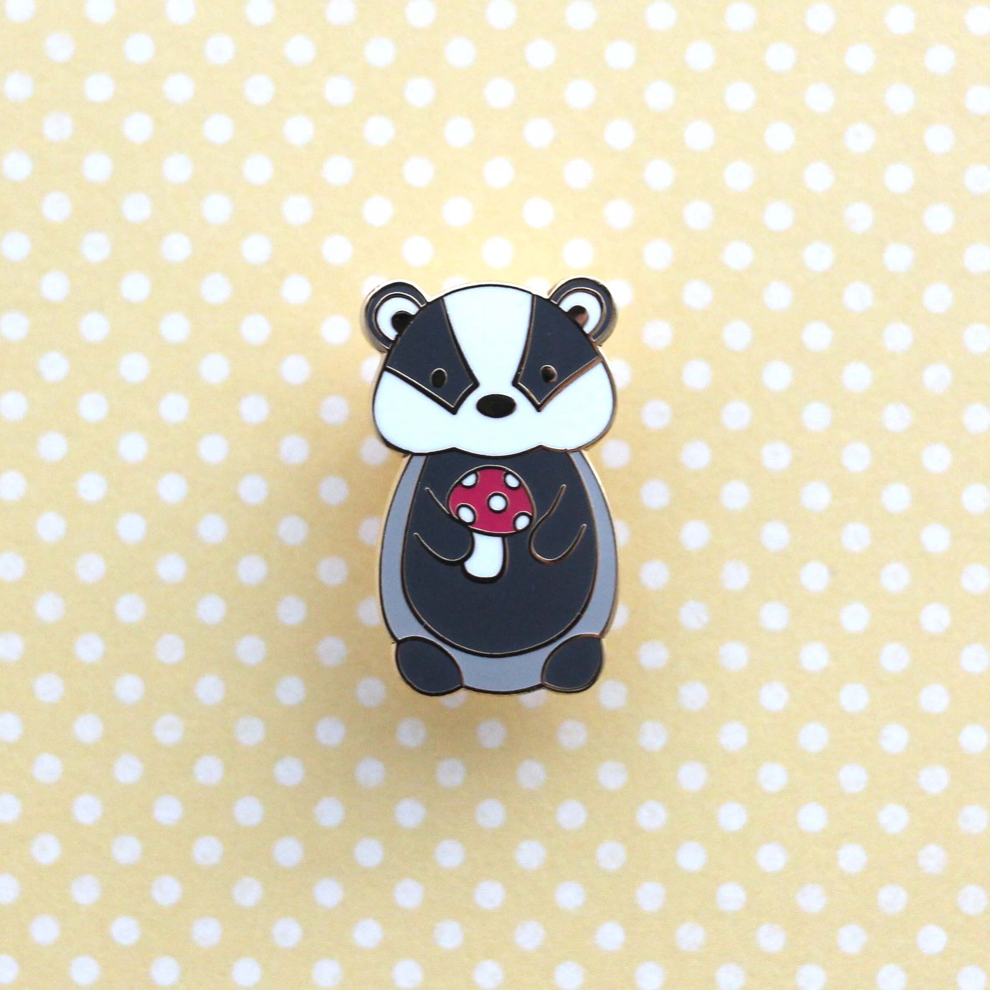 Badge en émail représentant un blaireau tenant un champignon rouge. Badge animal des bois.