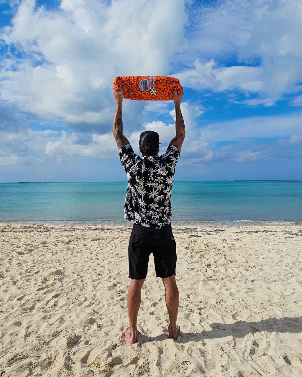 Man standing on the beach holding a packed Suniela beach cabana overhead, showing its compact and lightweight design