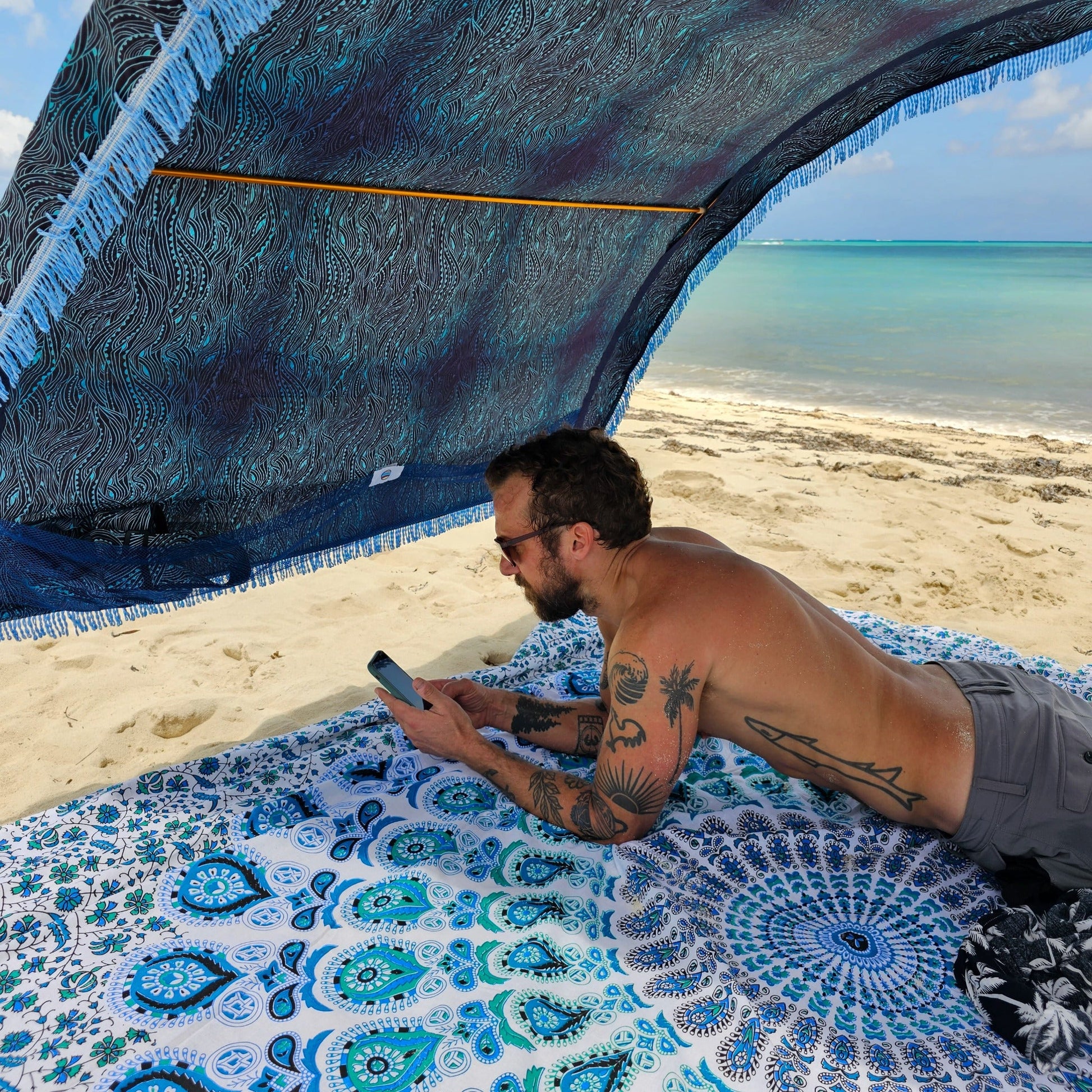 Man using his phone beneath a Suniela portable beach cabana with Ocean Waves cotton canopy on a sandy beach