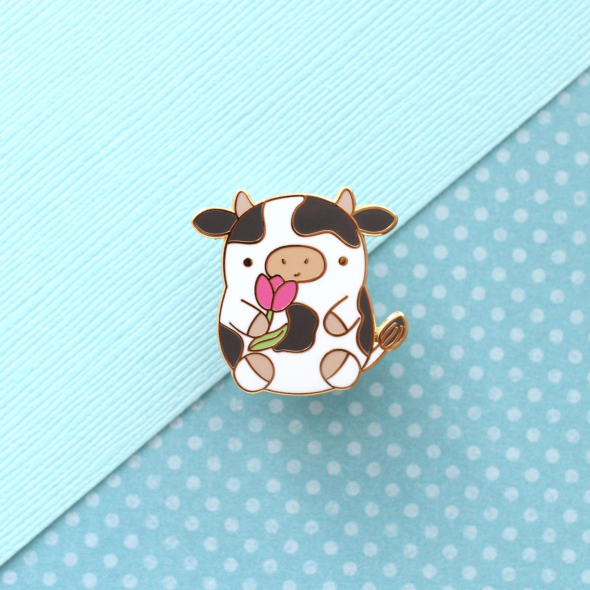 Pin's en émail représentant une vache. Jolie vache tenant une tulipe. Pin's kawaii.