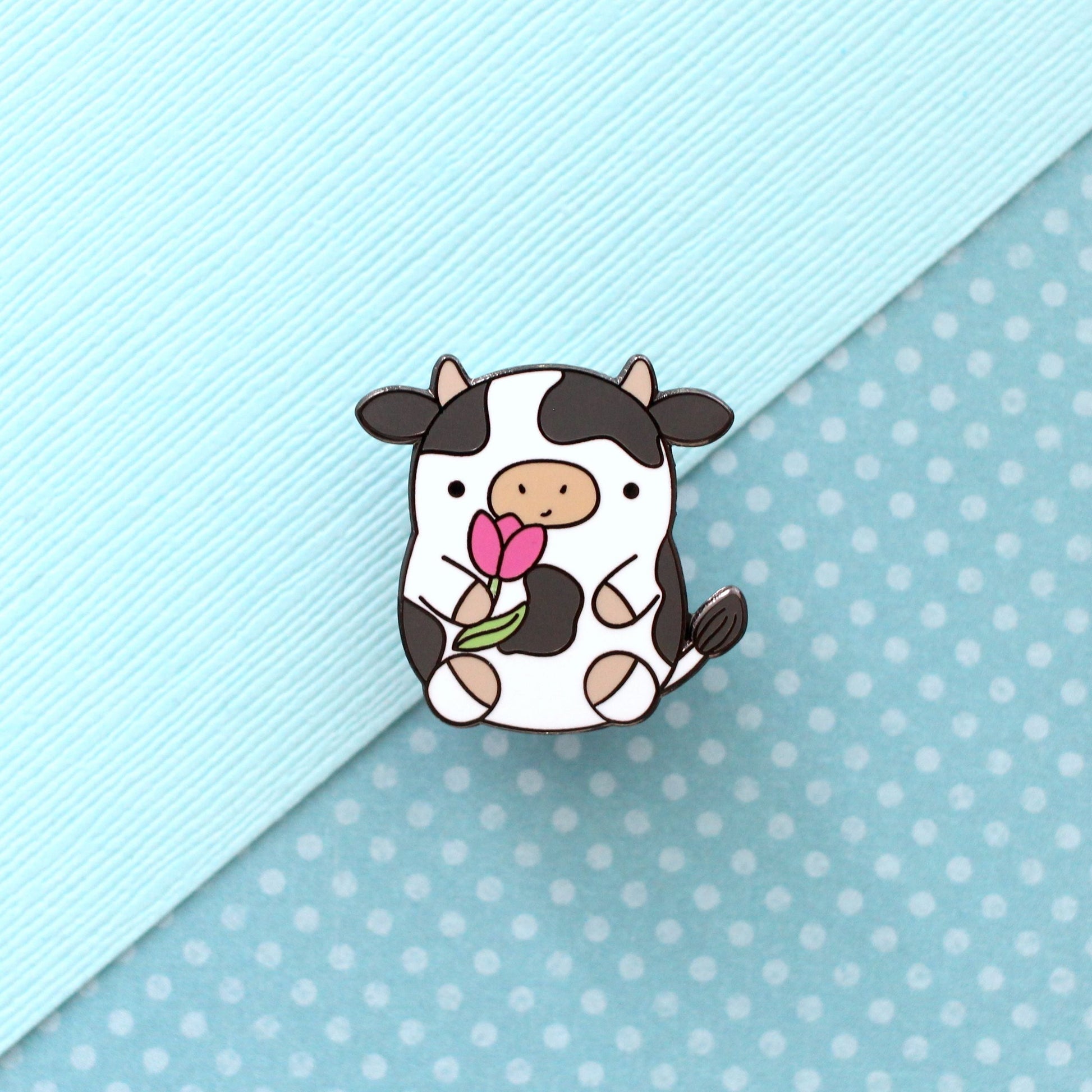 Pin's en émail représentant une vache. Jolie vache tenant une tulipe. Pin's kawaii.