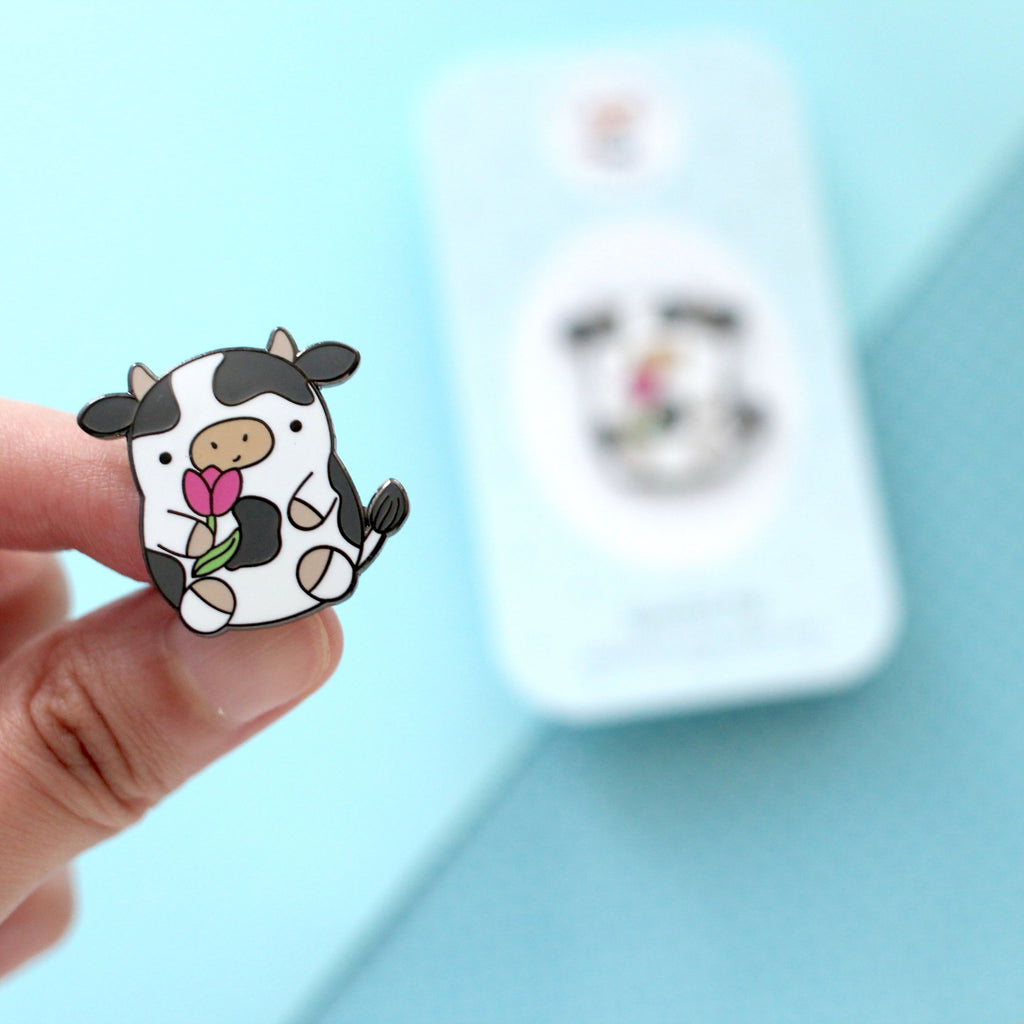 Pin's en émail représentant une vache. Jolie vache tenant une tulipe. Pin's kawaii.