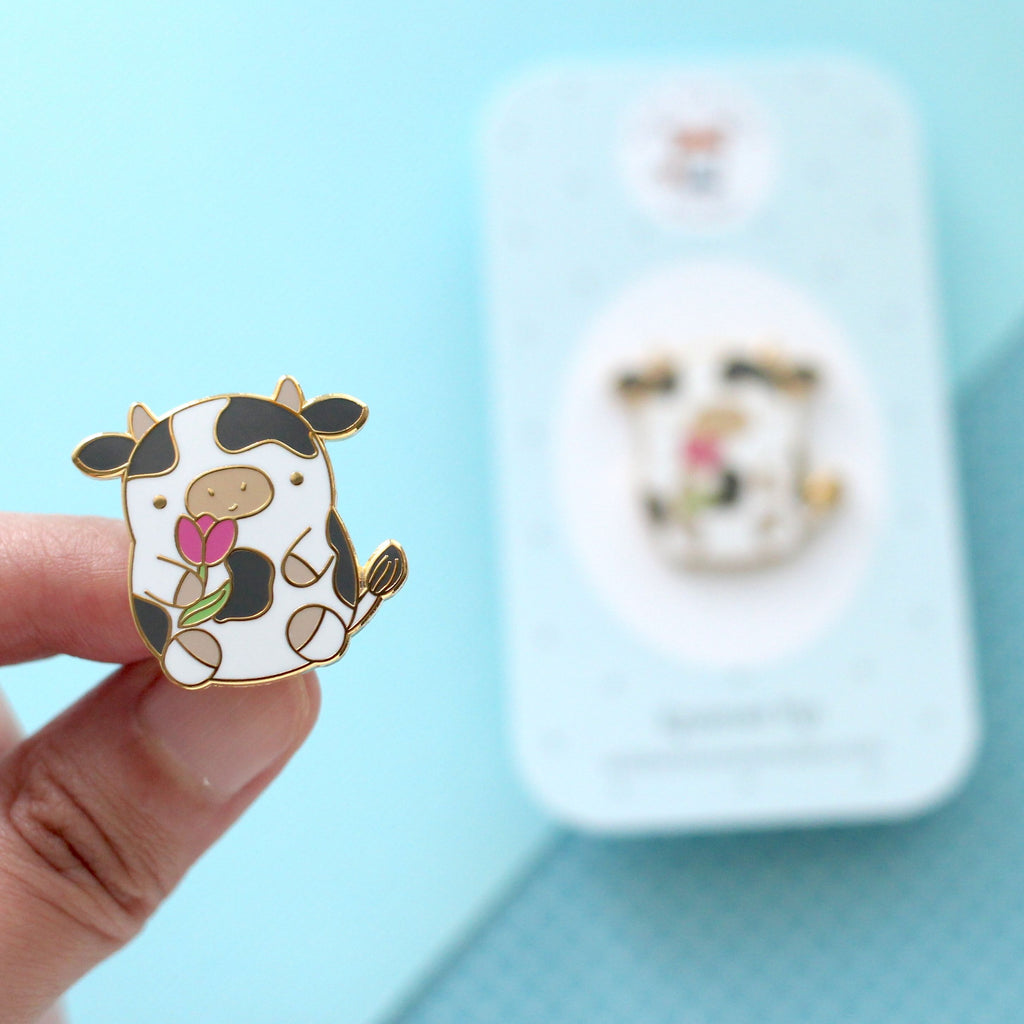 Pin's en émail représentant une vache. Jolie vache tenant une tulipe. Pin's kawaii.