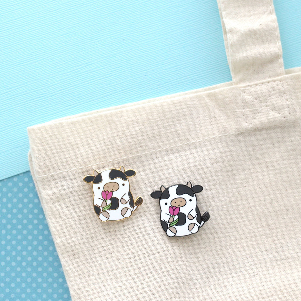 Pin's en émail représentant une vache. Jolie vache tenant une tulipe. Pin's kawaii.