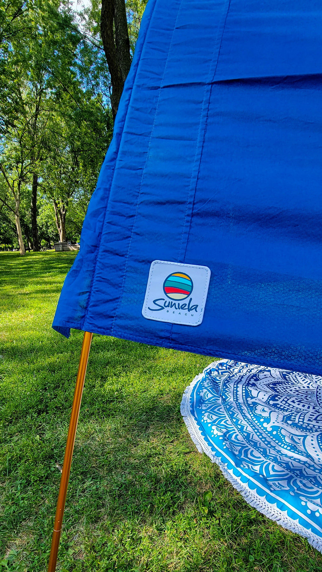 A close-up of a blue Suniela cotton canopy with its gold support pole on a grassy lawn.