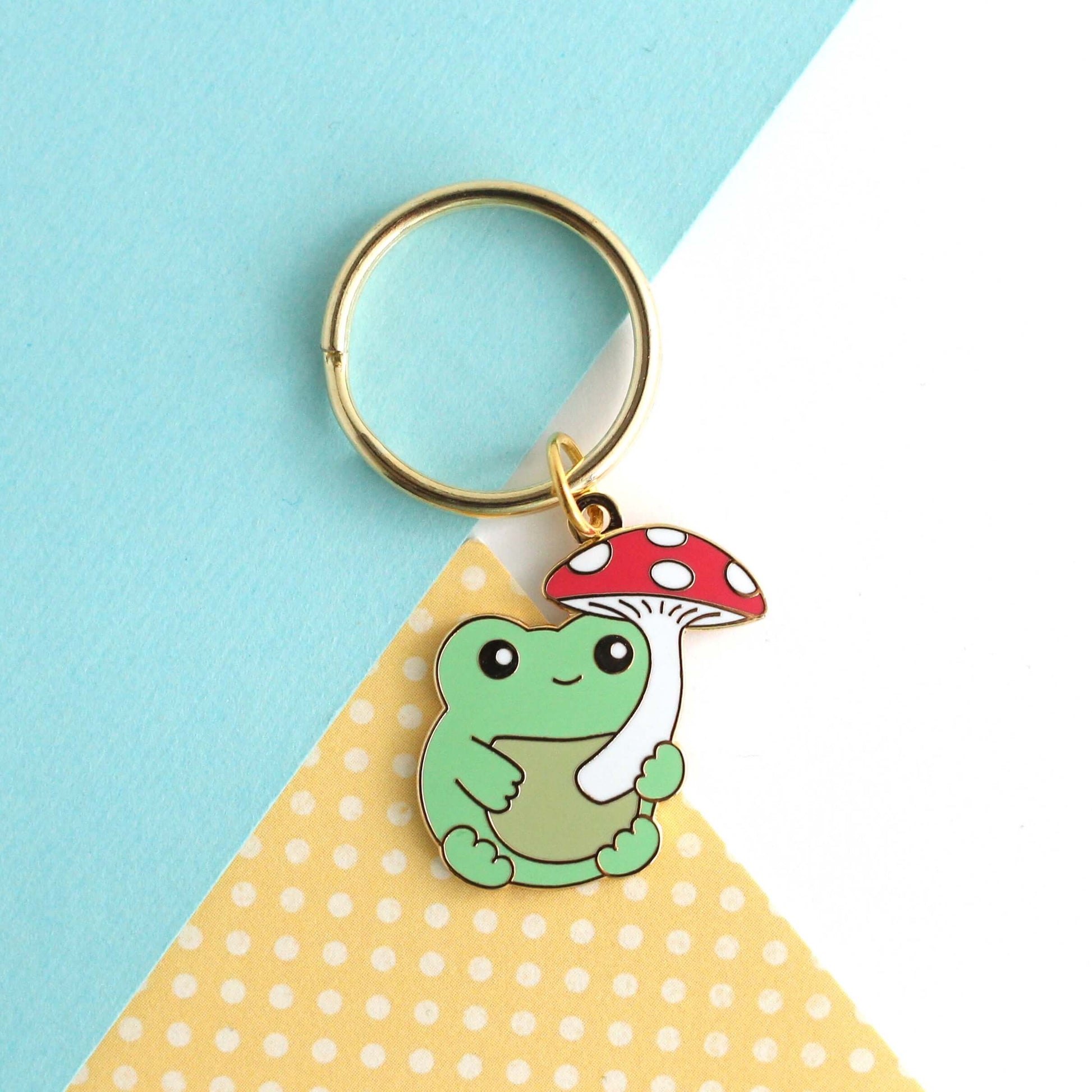 Porte-clés en émail représentant une grenouille avec un parapluie en forme de champignon rouge