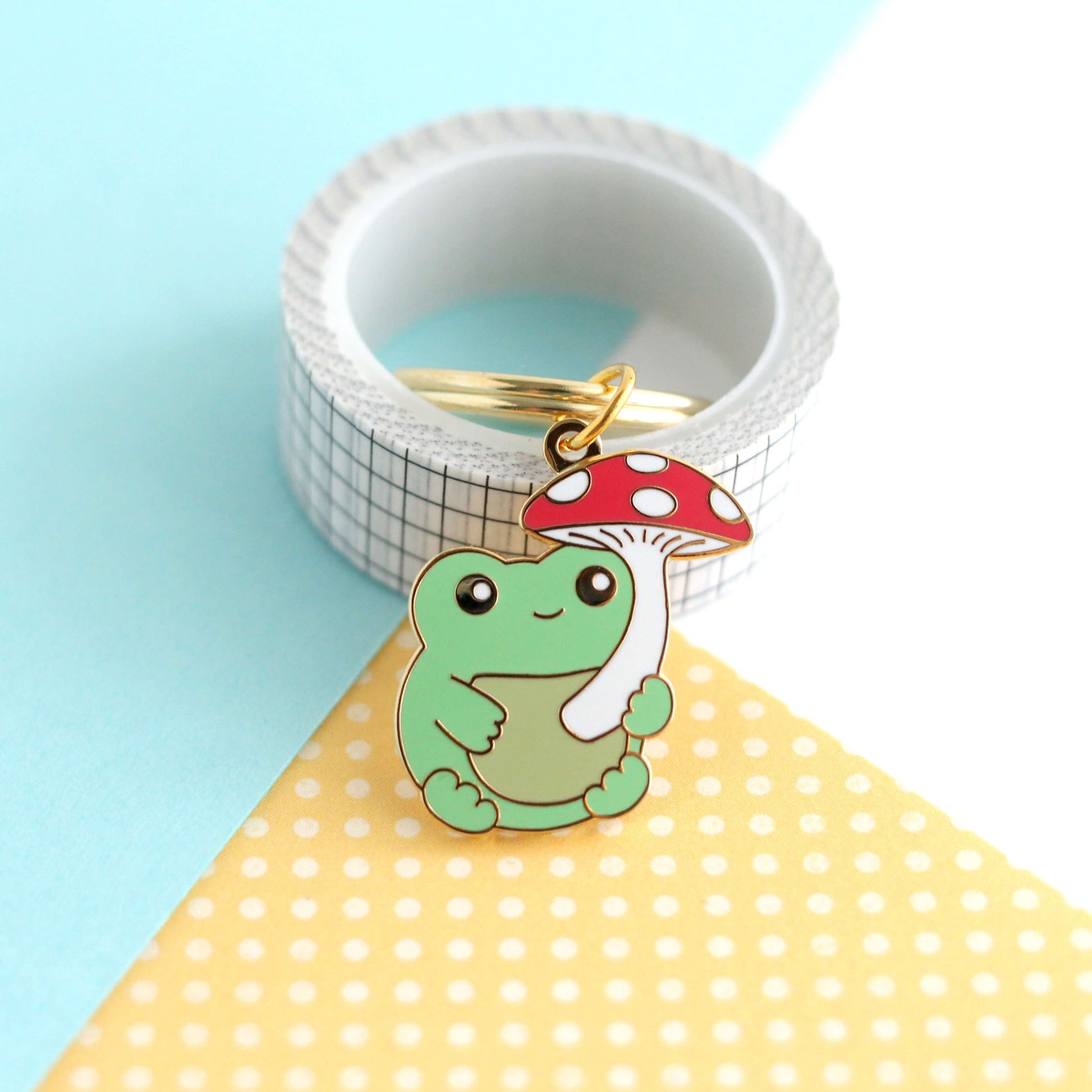 Porte-clés en émail représentant une grenouille avec un parapluie en forme de champignon rouge