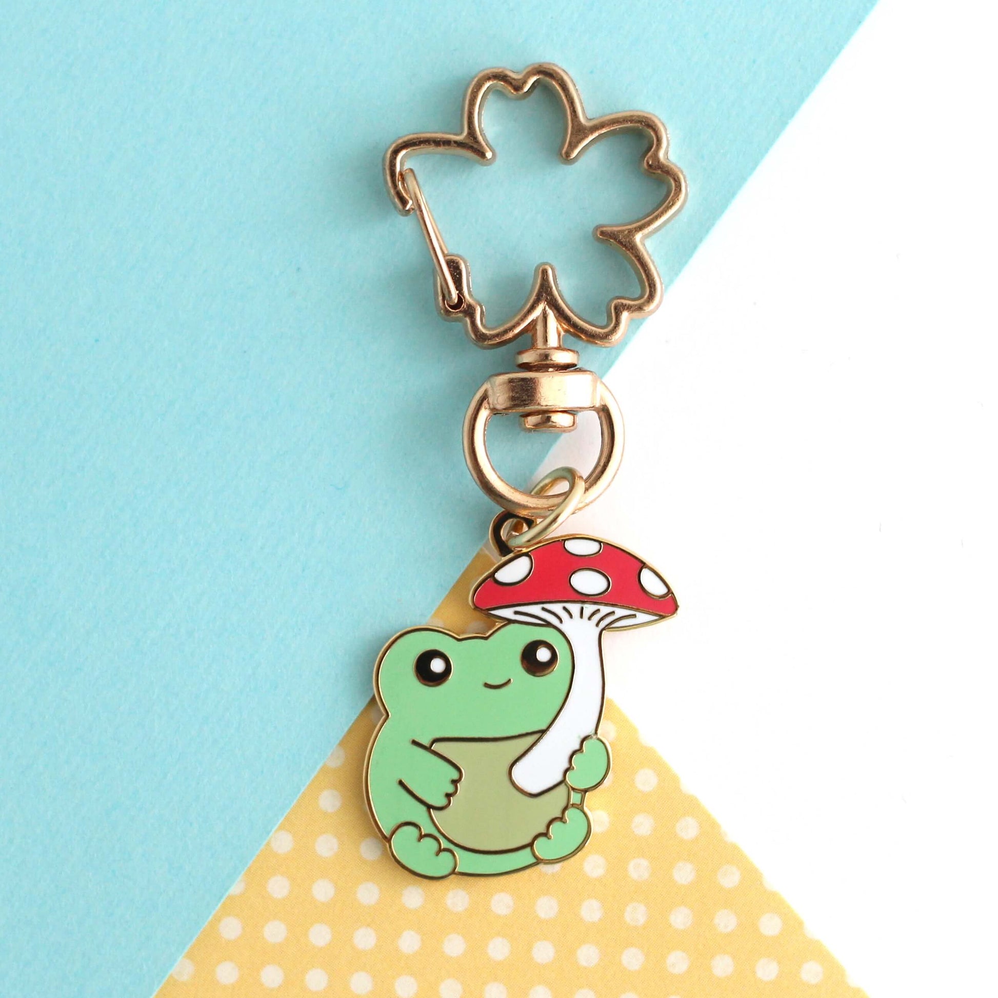 Porte-clés en émail représentant une grenouille avec un parapluie en forme de champignon rouge