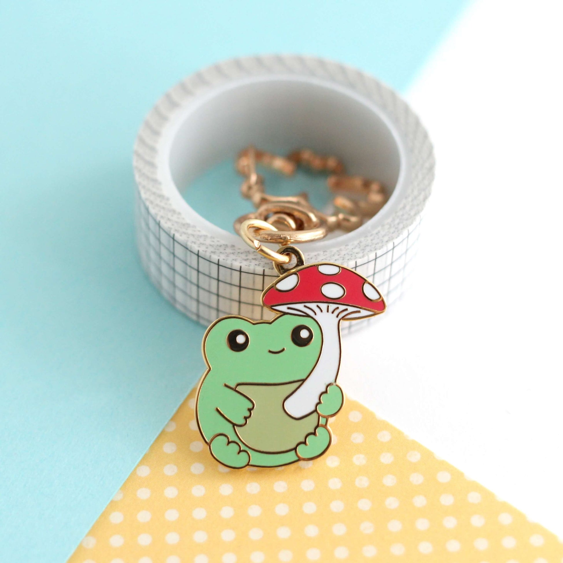 Porte-clés en émail représentant une grenouille avec un parapluie en forme de champignon rouge