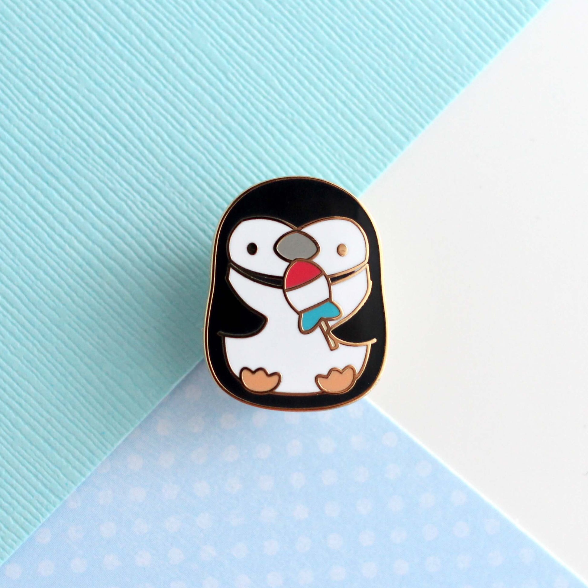 Pin's en émail représentant un pingouin à jugulaire tenant un poisson-fusée