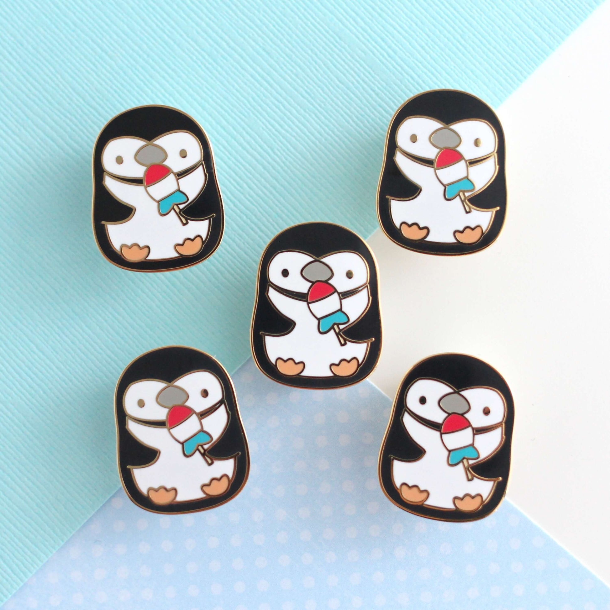 Pin's en émail représentant un pingouin à jugulaire tenant un poisson-fusée