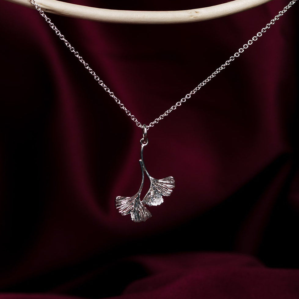 Silver necklace with two ginkgo leaves on a dark red fabric background