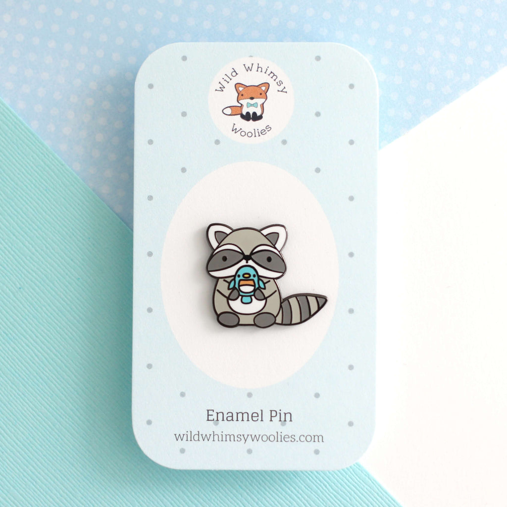 Broche en émail représentant un raton laveur tenant un oiseau bleu
