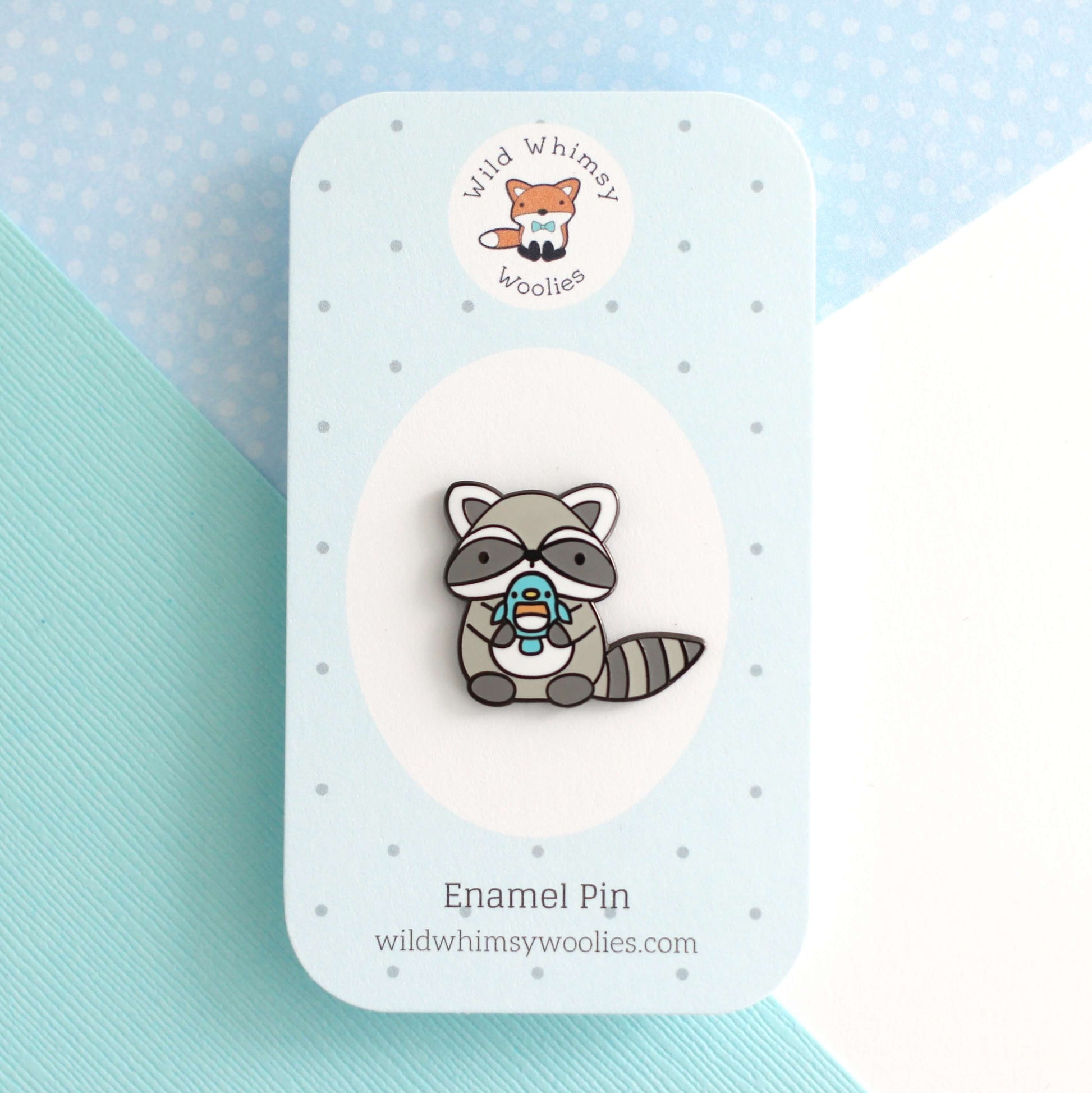 Broche en émail représentant un raton laveur tenant un oiseau bleu