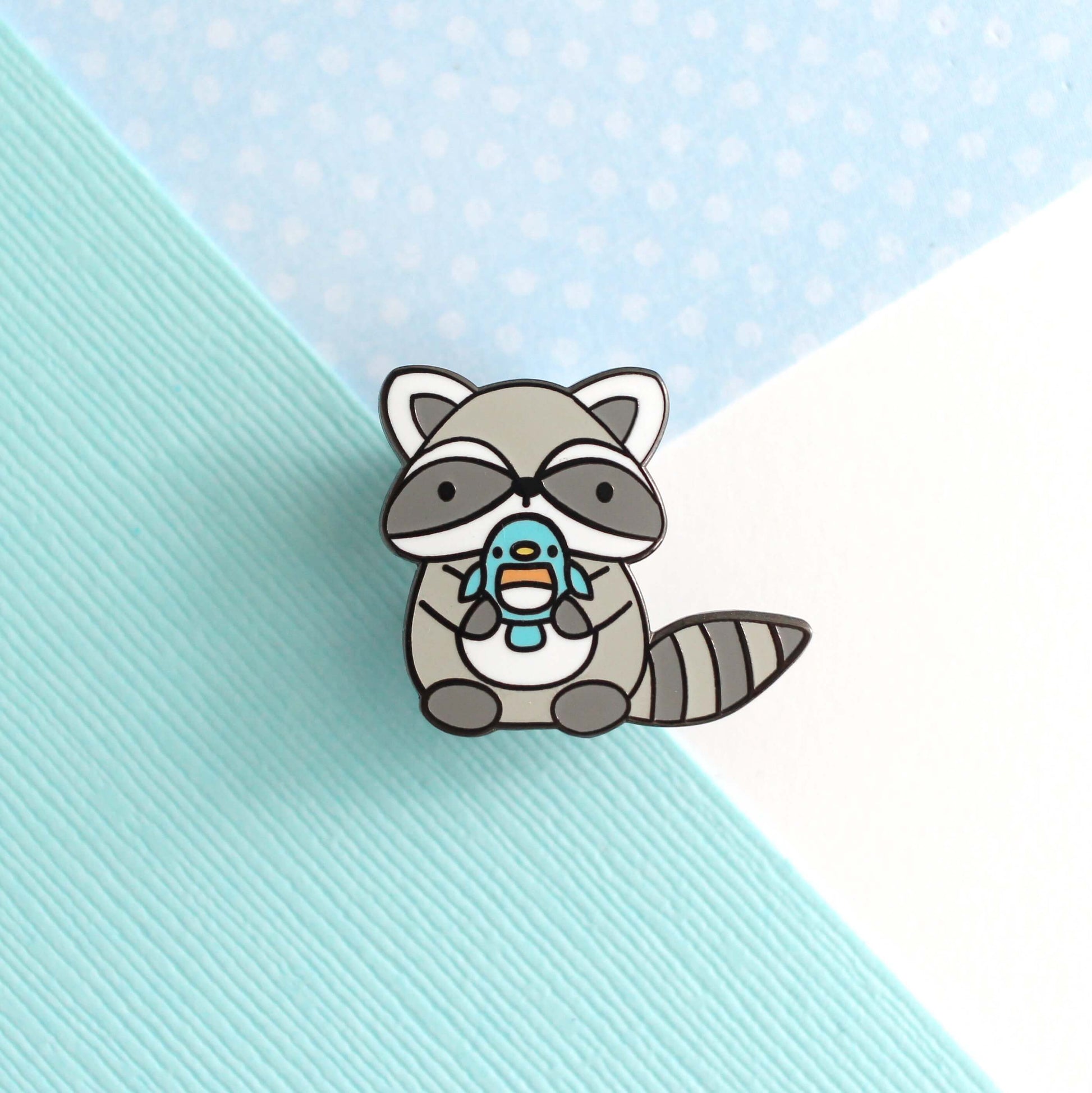 Broche en émail représentant un raton laveur tenant un oiseau bleu
