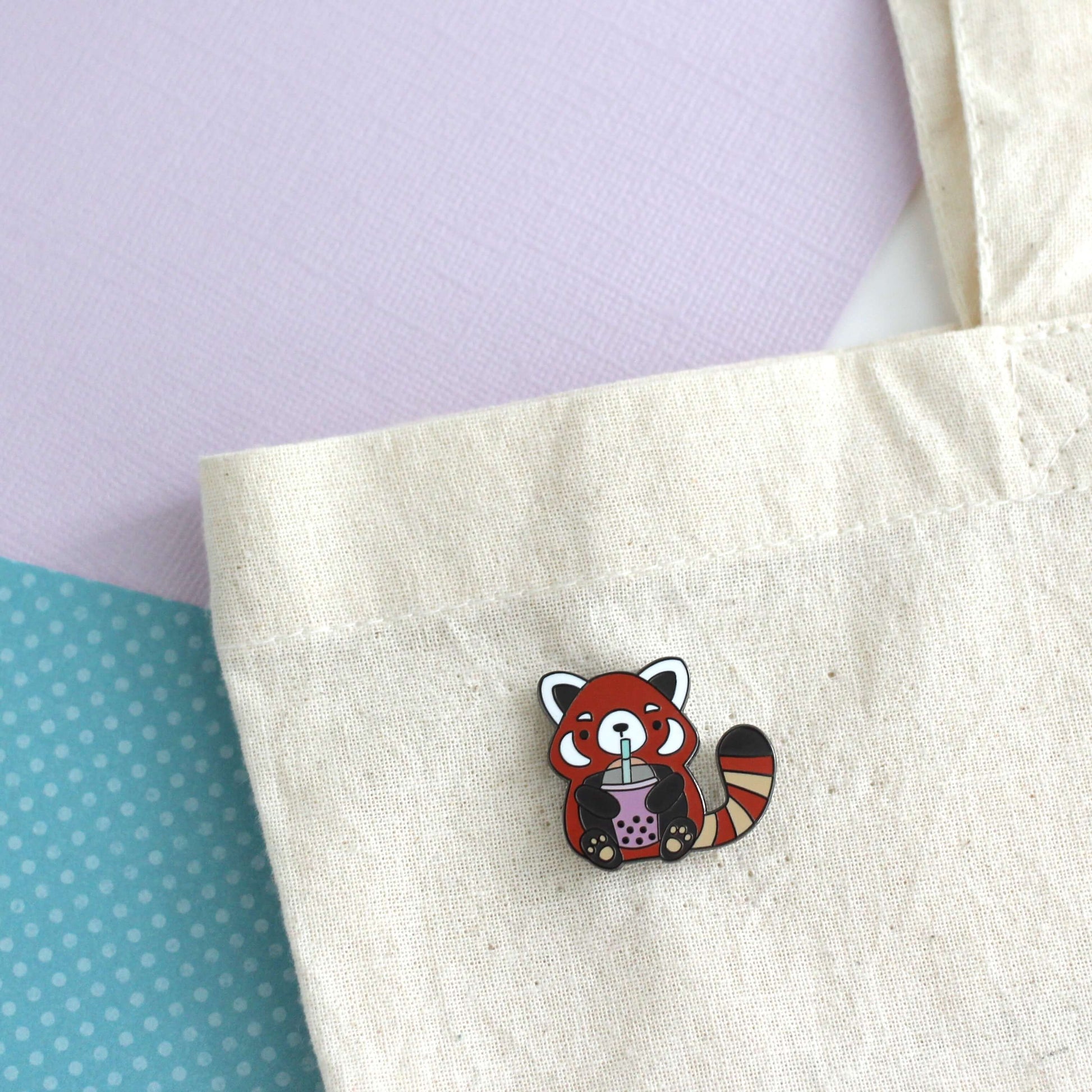 Pin's en émail représentant un panda roux buvant du thé aux perles. Cadeau pour les amateurs de thé aux perles.