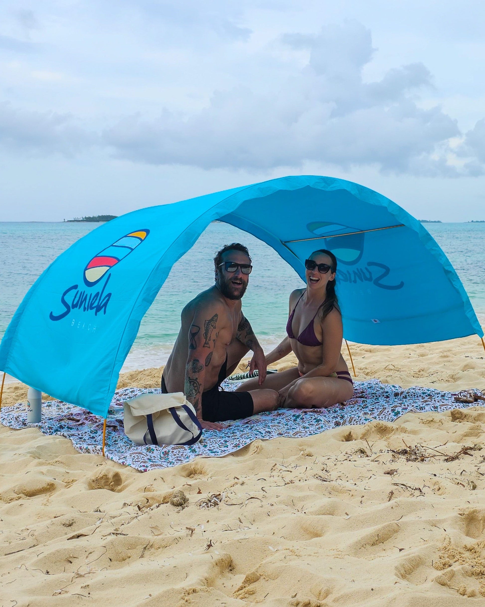 Couple sitting beneath an arched, blue Suniela shade cabana on a sandy beach