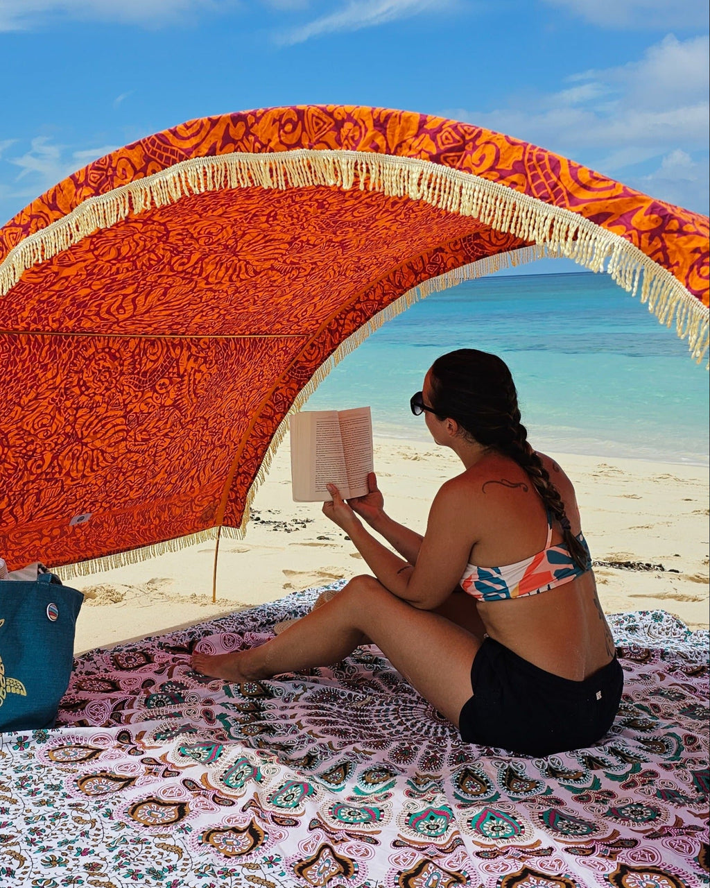 Woman reading beneath a Suniela beach cabana featuring the Tribal Jungle cotton canopy with decorative fringe