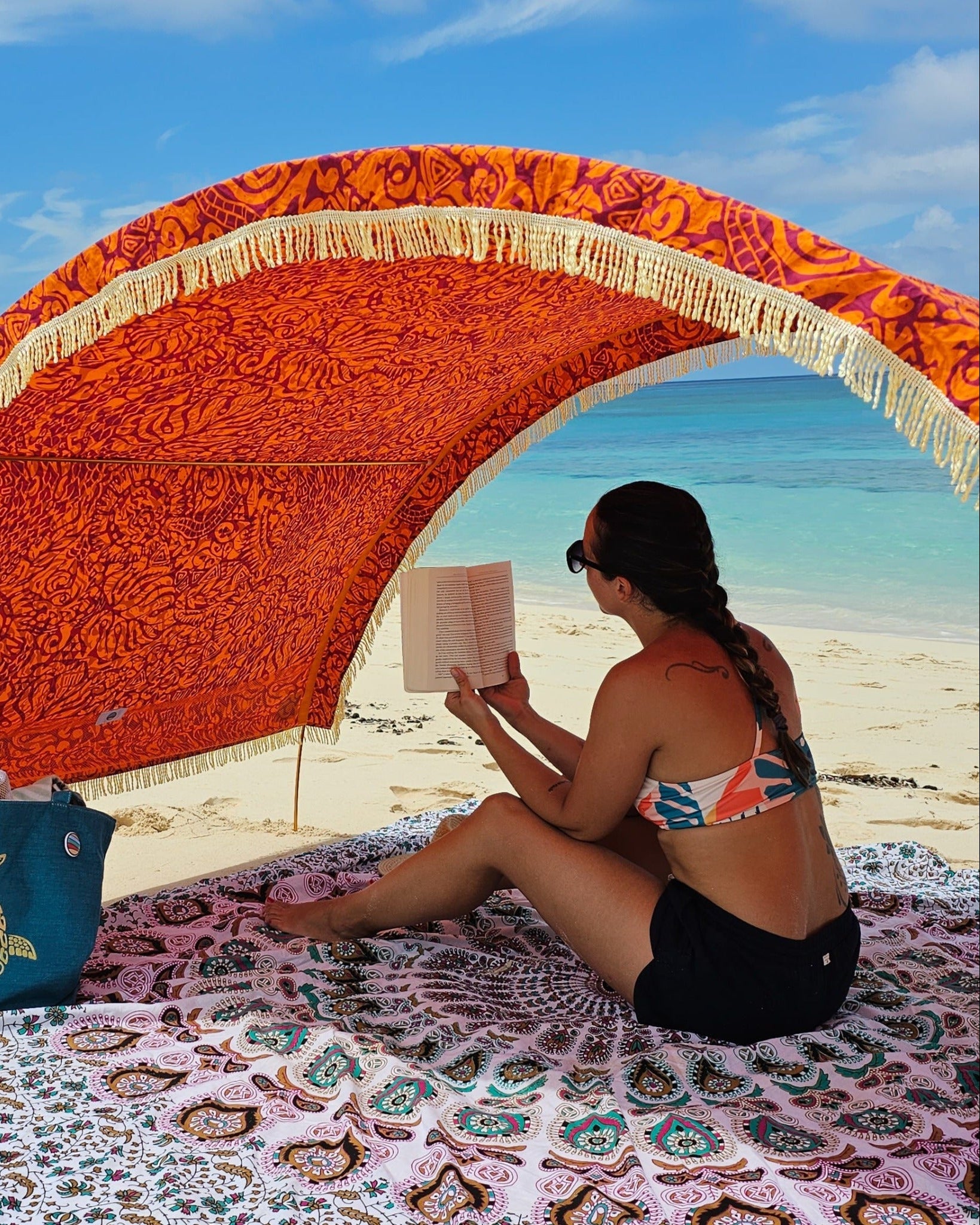 Woman reading beneath a Suniela beach cabana featuring the Tribal Jungle cotton canopy with decorative fringe