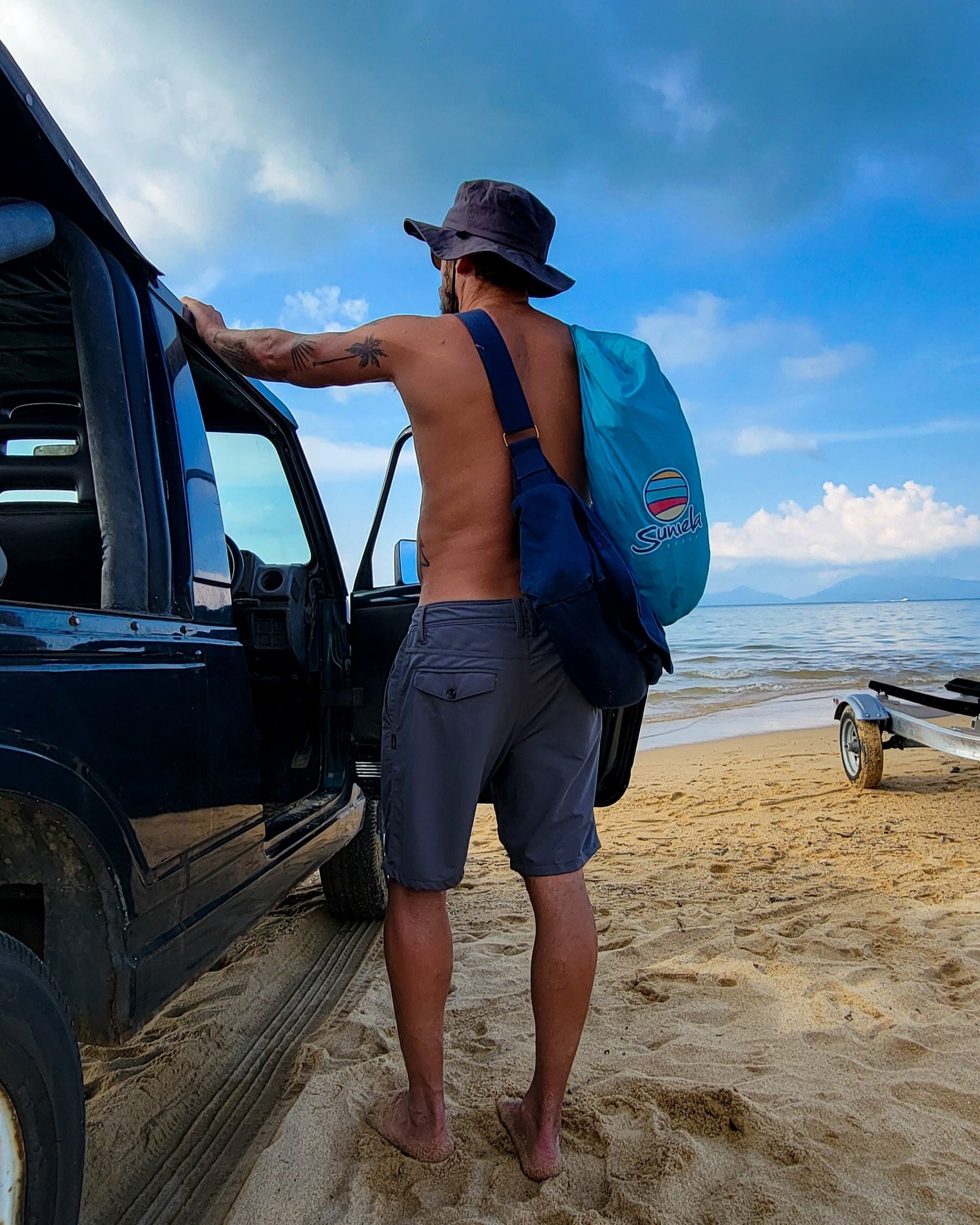 Man standing by a Jeep on a sandy beach carrying a Suniela portable beach cabana in its compact carry bag