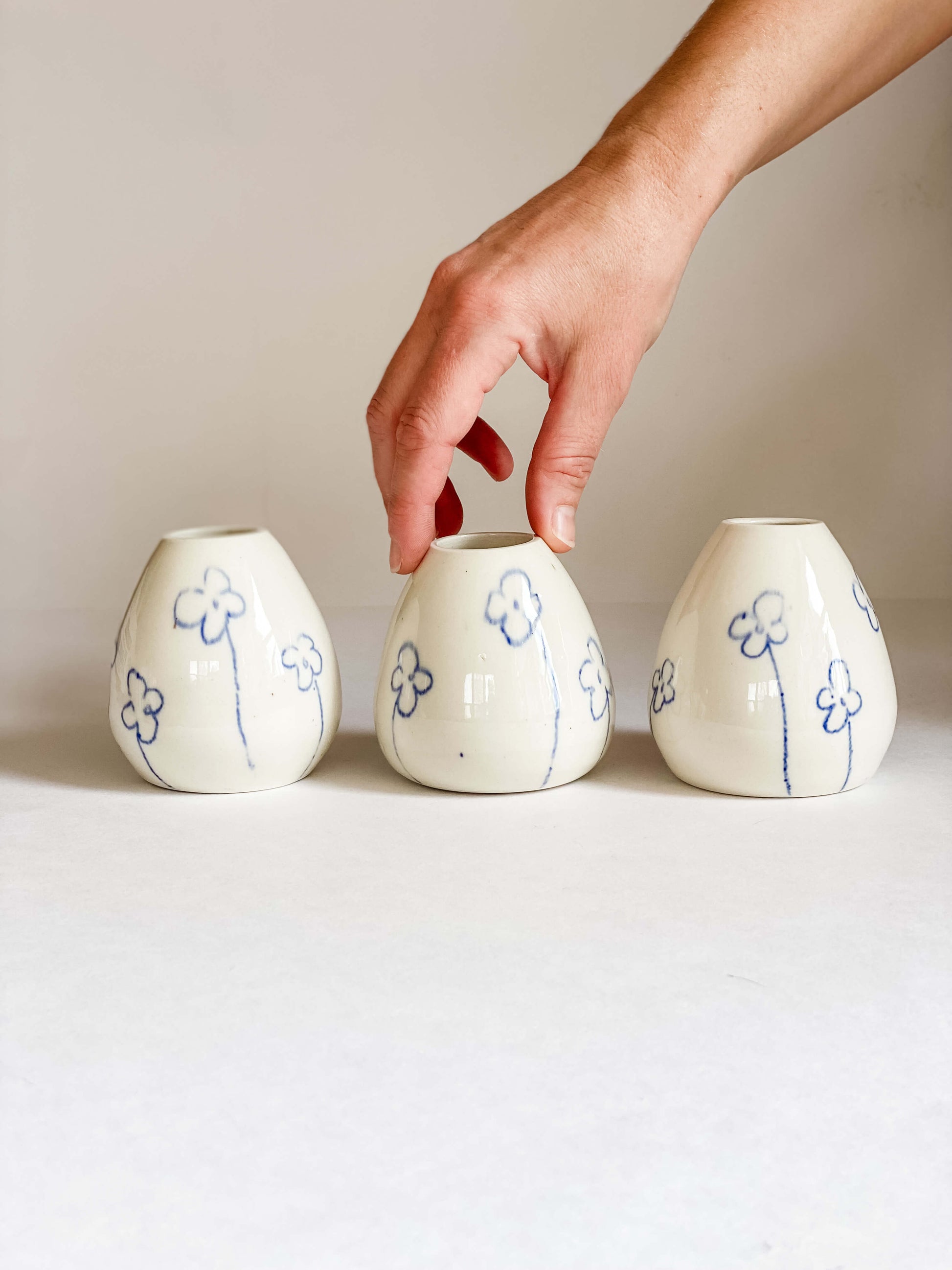 handmade pottery pear shaped white porcelain bud vase hand drawn blue flowers with white hand for scale