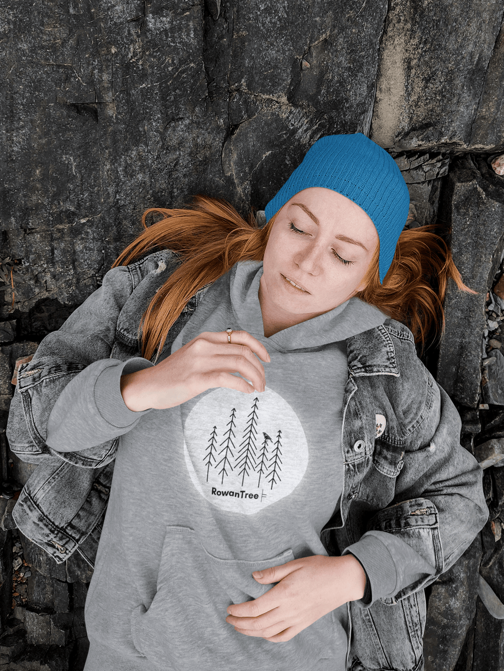 Young woman laying on rocks, wearing a heather grey hoodie with a moonlit grove 