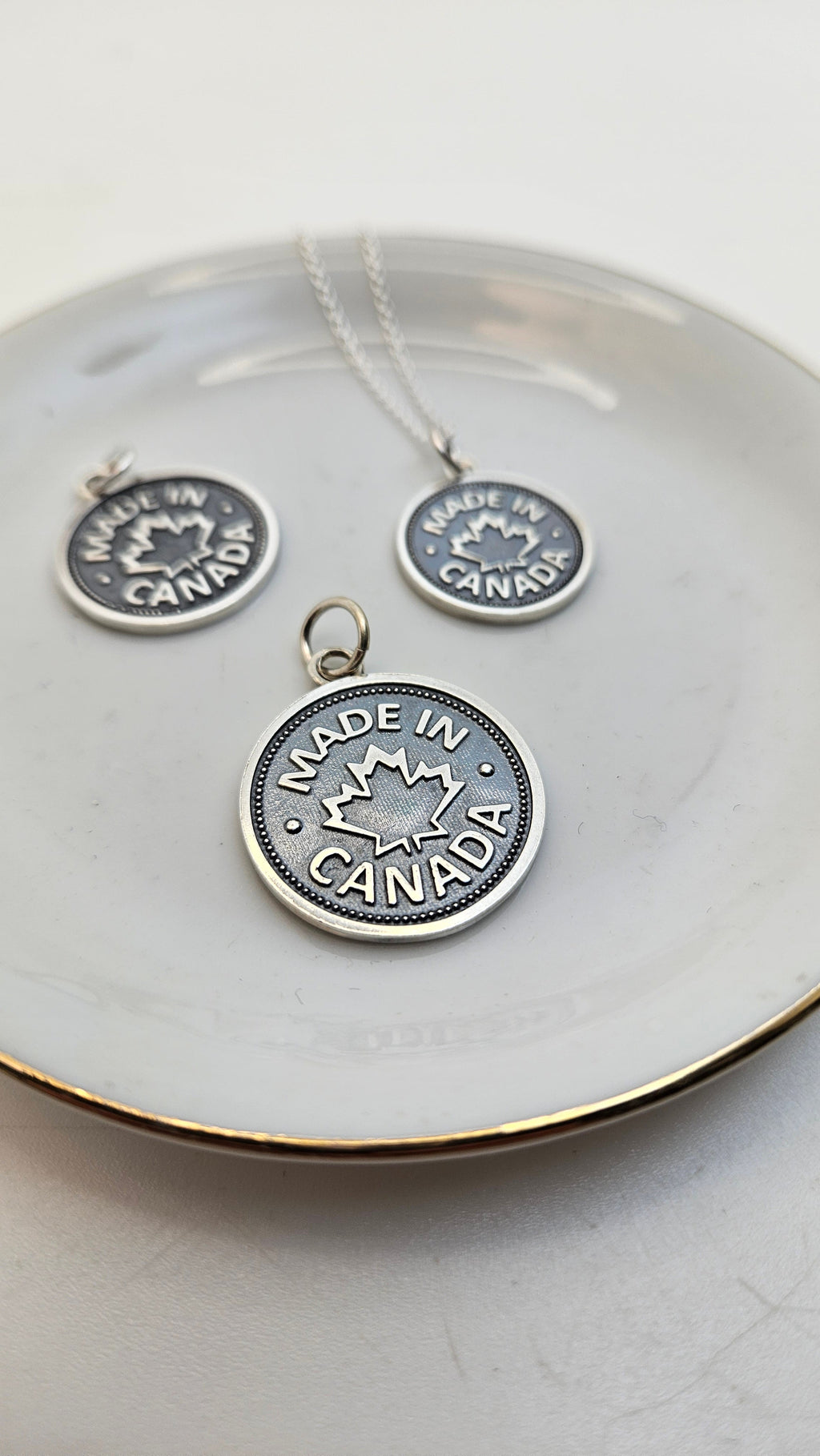 Three sterling silver coin pendants of different sizes with a 'MADE IN CANADA' inscription and a maple leaf design, displayed on a white plate.