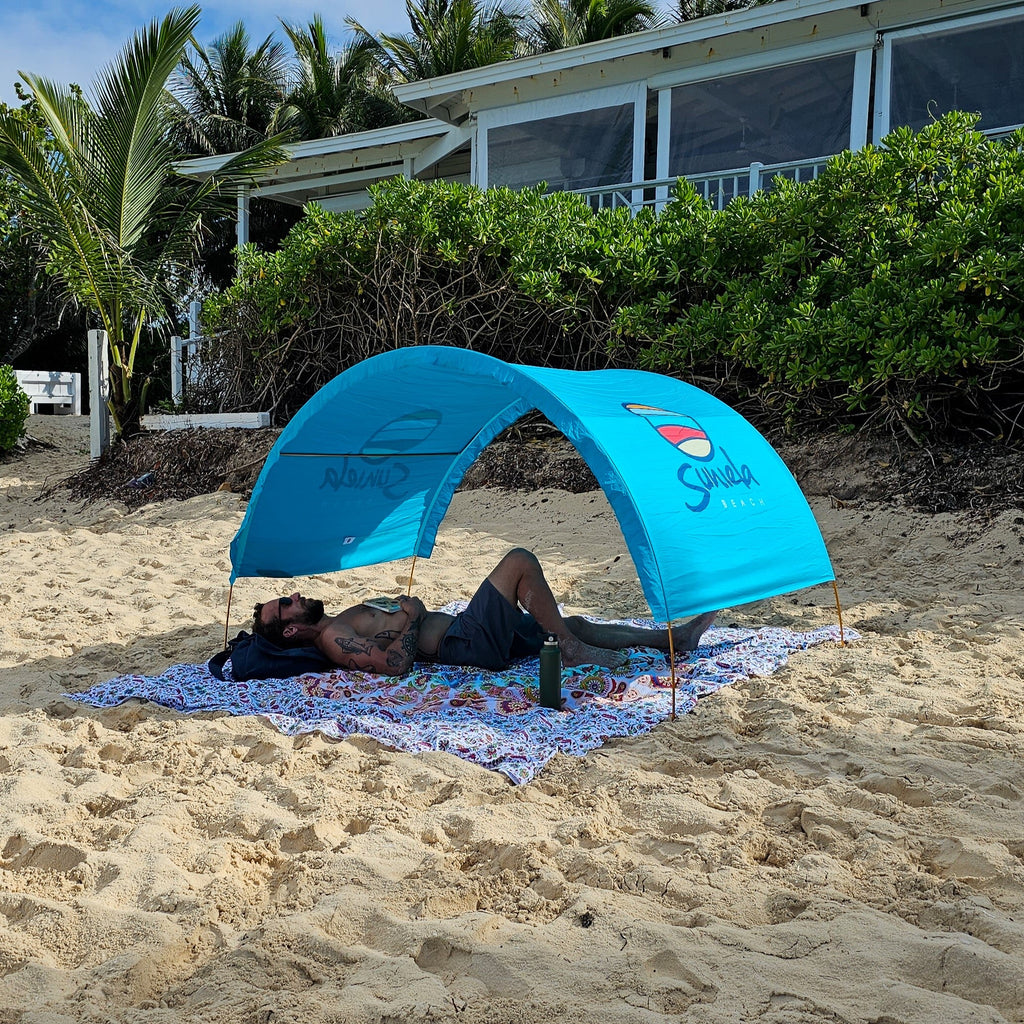 Man relaxing under a turquoise Suniela portable beach cabana on a sandy beach