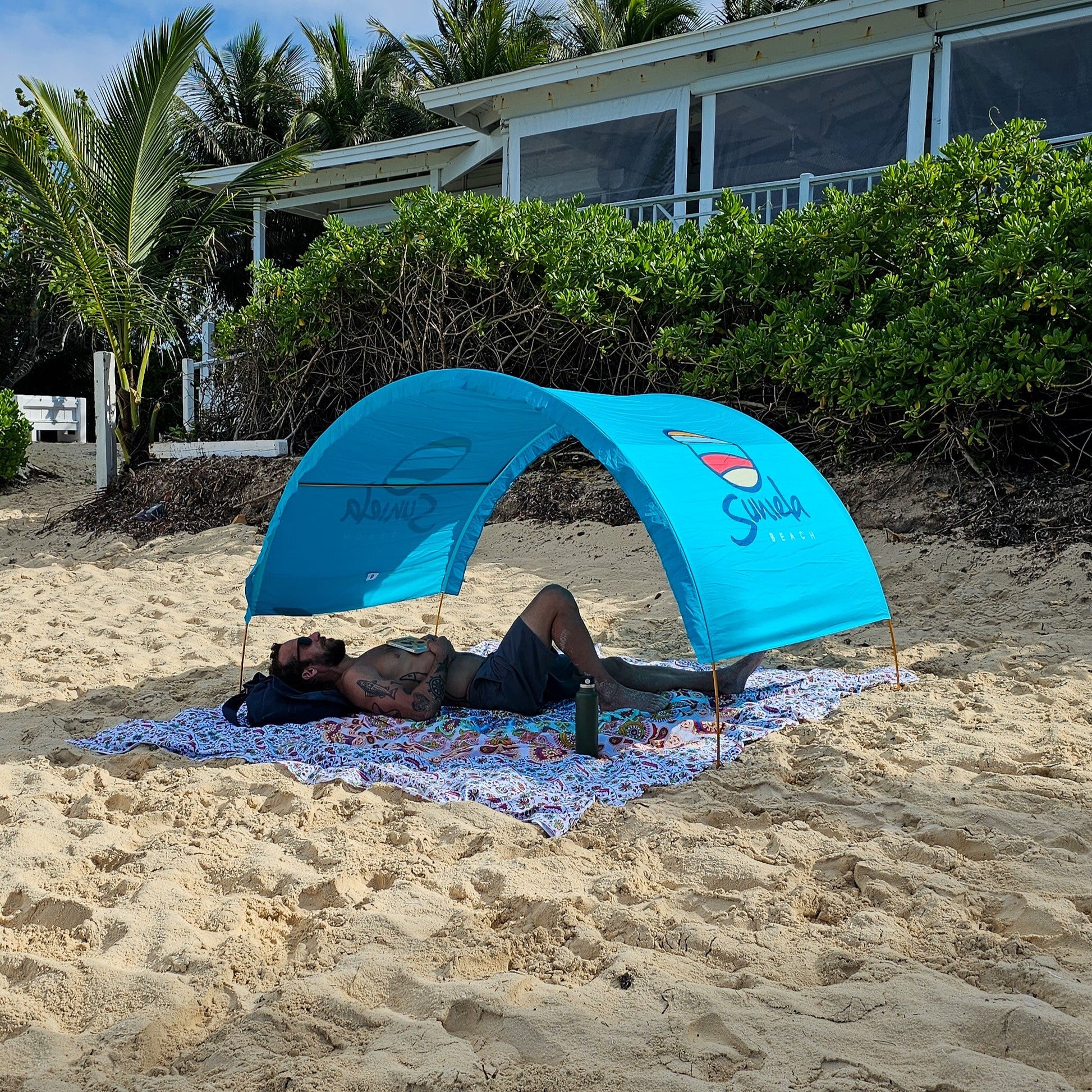 Man relaxing under a turquoise Suniela portable beach cabana on a sandy beach