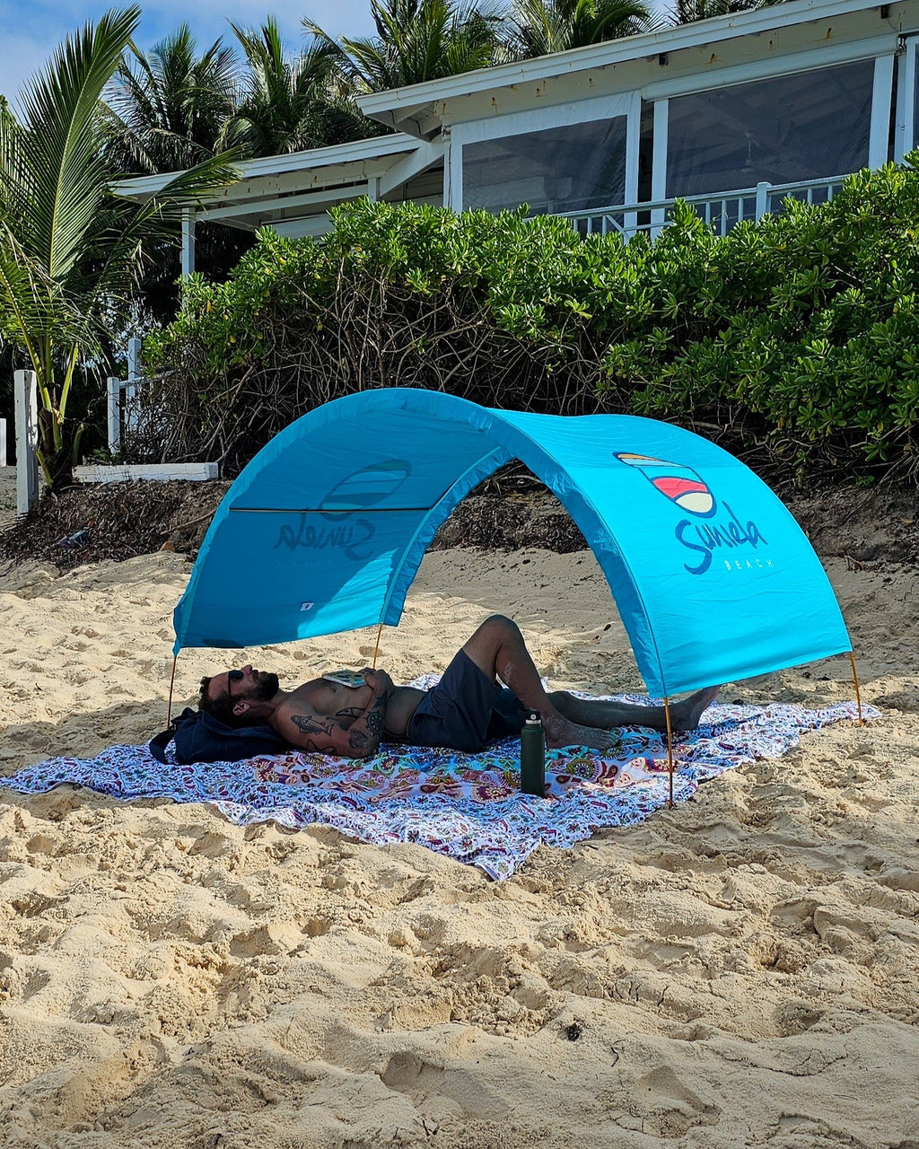 Man relaxing under a turquoise Suniela portable beach cabana on a sandy beach